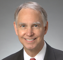 A middle-aged man with gray hair, wearing a dark suit, white shirt, and red tie, smiles at the camera against a plain gray background—exuding the professionalism often seen among top lawyers in Chicago.