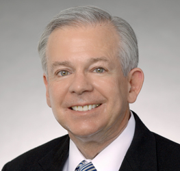 Smiling older man with short gray hair in a dark suit, white shirt, and striped tie, posing in front of a plain light gray background—portraying confidence often seen among top lawyers in Chicago.
