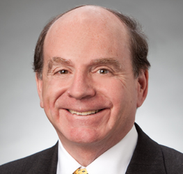 Middle-aged man with thinning hair wearing a dark suit, white shirt, and yellow patterned tie, smiling at the camera against a neutral background—ideal for profiles of lawyers in Chicago or a corporate law office.