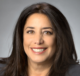 Woman with long dark hair, wearing a dark blazer, smiling at the camera against a neutral gray background—an ideal professional portrait for law offices or corporate law office teams in Chicago.