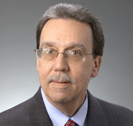 A middle-aged man with glasses, mustache, and gray hair, wearing a suit, tie, and striped shirt, poses in front of a neutral gray background—reflecting the professionalism found at law offices or among experienced lawyers in Chicago.