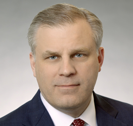 A man with short, light-colored hair in a dark suit, white shirt, and red tie poses for a professional headshot against a plain background, representing the corporate law office trusted by Chicago lawyers.