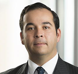 Man in a suit and tie with dark hair, facing forward in a professional setting at one of the leading law offices specializing in intellectual property law, with a blurred background.