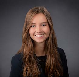 A woman with long brown hair, wearing a dark blazer and a necklace, smiles at the camera against a plain dark background—reflecting the professionalism of Chicago lawyers in a leading corporate law office.