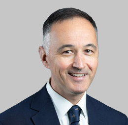 Man wearing a dark suit, white shirt, and dark tie, smiling at the camera against a plain light gray background—professional attire fit for Chicago lawyers specializing in intellectual property law.