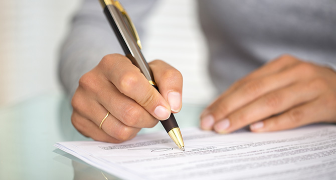 At a corporate law office, a person holding a pen signs a document on a glass table.