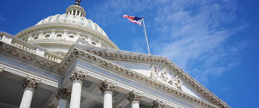 The United States Capitol building with columns and a dome, topped by an American flag against a blue sky—an inspiring symbol for law offices and those seeking litigation support.