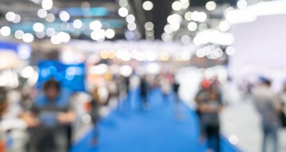 A blurred image of people walking and gathering in a brightly lit indoor event space with a blue carpet, reminiscent of a corporate law office or networking event for lawyers in Chicago.