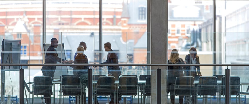A group of people are meeting around a conference table in a modern law office with large windows overlooking city buildings, discussing intellectual property law and litigation support.