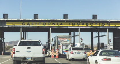 Vehicles waiting in line at a California Inspection station under a large yellow sign, with traffic cones and stoplights visible—much like clients awaiting guidance from Chicago lawyers skilled in intellectual property law.