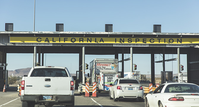 Vehicles waiting in line at a California Inspection station under a large yellow sign, with traffic cones and stoplights visible—much like clients awaiting guidance from Chicago lawyers skilled in intellectual property law.