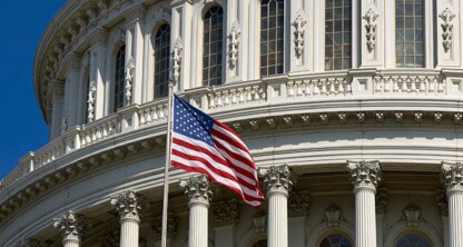 An American flag flies in front of the U.S. Capitol building, showing white columns, arched windows, and architectural details against a clear blue sky—an inspiring sight for Chicago lawyers practicing near law offices in the nation’s capital.
