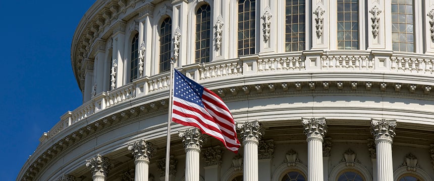 An American flag flies in front of the U.S. Capitol building, showing white columns, arched windows, and architectural details against a clear blue sky—an inspiring sight for Chicago lawyers practicing near law offices in the nation’s capital.