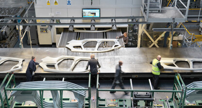 Five workers stand around a large metal table handling car body panels in an automotive manufacturing facility, much like a team providing litigation support in law offices or managing intellectual property law cases with precision and teamwork.
