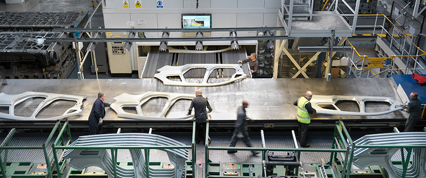 Five workers stand around a large metal table handling car body panels in an automotive manufacturing facility, much like a team providing litigation support in law offices or managing intellectual property law cases with precision and teamwork.