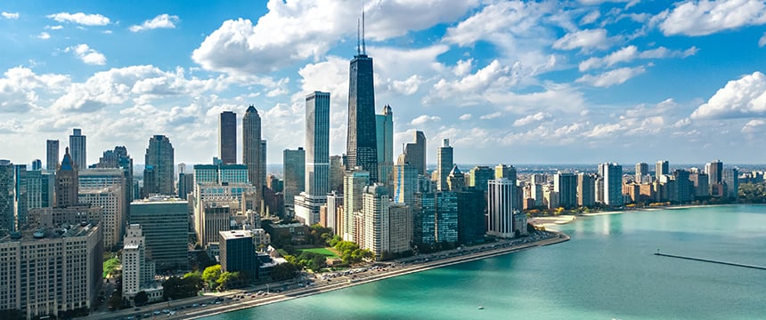 Aerial view of a city skyline with tall buildings, including prominent law offices, next to a large body of water under a partly cloudy sky.