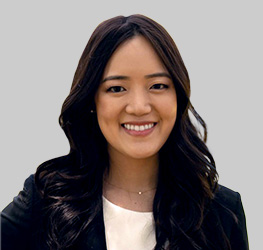 Woman with long dark hair smiling, wearing a black blazer over a white top, posed against a plain light gray background—perfect for professional law offices or profiles specializing in intellectual property law.
