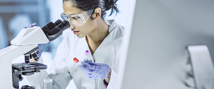 A scientist wearing safety goggles and gloves examines a sample under a microscope, reflecting the precision seen in intellectual property law practices within top law offices.