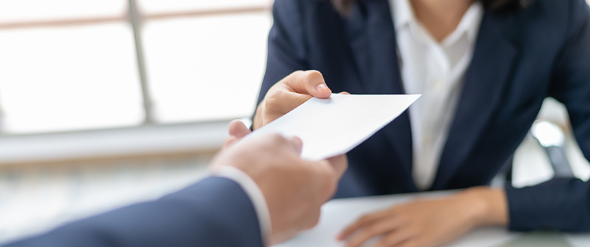 A person in a suit hands an envelope to another individual across a table, capturing a moment often seen in law offices with chicago lawyers handling important legal matters.