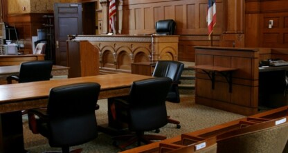 Empty courtroom with wooden desks, black chairs, a judge's bench, witness stand, and American flag; no people present—an atmosphere familiar to lawyers in Chicago and nearby law offices.