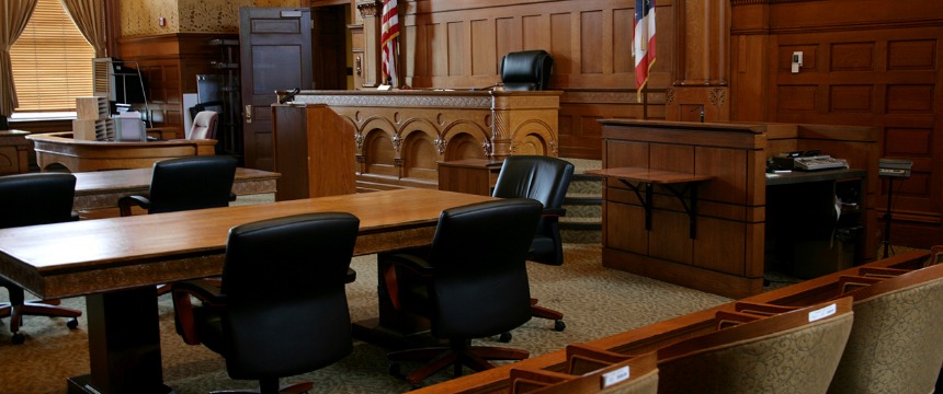 Empty courtroom with wooden desks, black chairs, a judge's bench, witness stand, and American flag; no people present—an atmosphere familiar to lawyers in Chicago and nearby law offices.