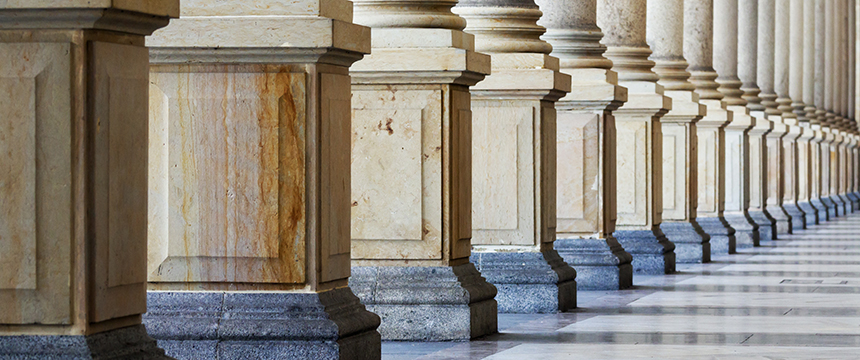 A row of stone columns with square bases and fluted shafts stands along a marble floor in an architectural colonnade, evoking the timeless elegance found in prestigious Chicago law offices.