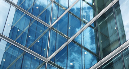 Close-up view of a modern glass office building facade reflecting blue sky and clouds, with geometric lines and window frames intersecting—an inspiring scene where top Chicago lawyers provide expert litigation support.