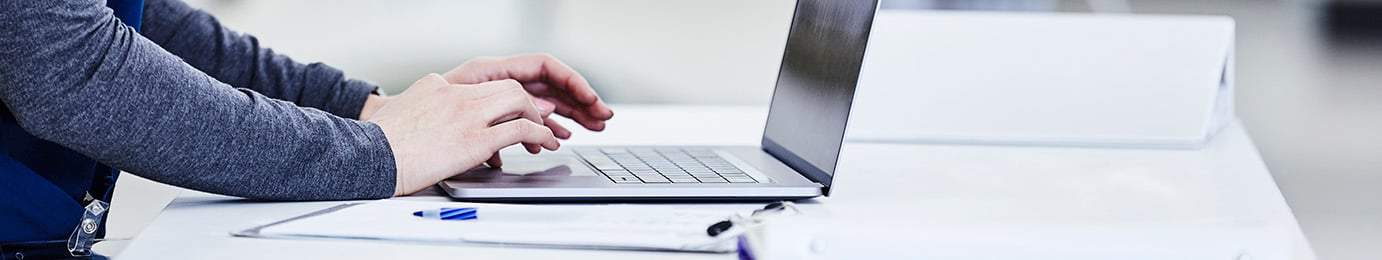 Person typing on a laptop at a white desk with a clipboard and papers nearby in a bright, modern corporate law office, ideal for litigation support and lawyers in Chicago.