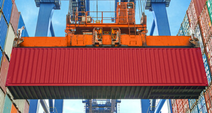 A large red shipping container is being lifted by an orange crane at a shipping port, surrounded by stacked colorful containers—much like law offices in Chicago navigating complex logistics with expert litigation support.