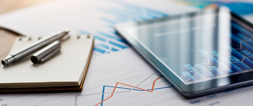 A tablet, a notepad with two pens, and papers with financial charts and graphs are arranged on a desk—an organized setup often seen in law offices of Chicago lawyers.