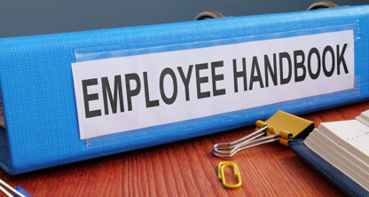 A blue binder labeled "Employee Handbook" sits on a desk at one of the law offices in Chicago, next to paper clips and an open notebook.