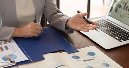 A person in business attire gestures toward a laptop displaying charts and graphs, with printed financial documents spread out on a wooden desk—ideal for chicago lawyers needing litigation support.