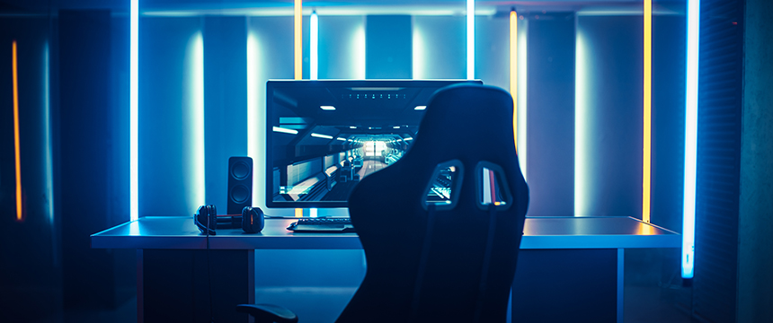 A modern gaming setup with a large monitor, speakers, headset, keyboard, and a gaming chair—illuminated by blue and yellow LED lights—would stand out even in the sleekest corporate law office.