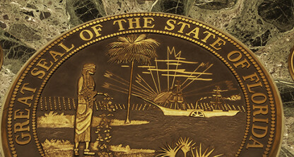 Bronze Great Seal of the State of Florida embedded in a green marble surface, surrounded by rope barriers and two smaller bronze medallions—a distinguished display often seen in prestigious law offices.