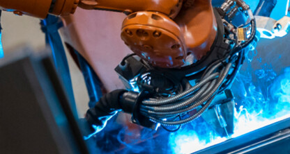 Close-up of an industrial robotic arm performing welding, with blue sparks and cables visible—much like the precision found in top corporate law offices handling complex cases.