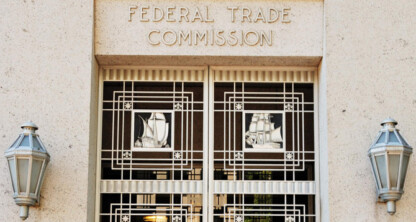Entrance of the Federal Trade Commission building with decorative metal doors featuring ship designs and two wall lanterns, representing the authority behind intellectual property law.