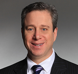 A man with short grayish hair wearing a dark pinstripe suit, white shirt, and striped tie, smiling against a plain gray background—capturing the professionalism of a leading corporate law office.
