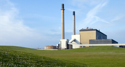 A power plant with two tall smokestacks stands behind a grassy field under a partly cloudy sky, much like law offices providing diligent litigation support amid the landscape of intellectual property law.