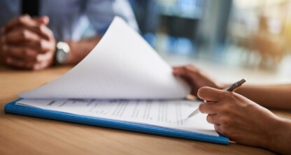 A person reviews and signs documents on a clipboard at a table, while another—perhaps from one of the leading Chicago lawyers or law offices—sits across with hands folded.