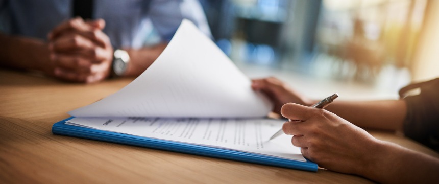 A person reviews and signs documents on a clipboard at a table, while another—perhaps from one of the leading Chicago lawyers or law offices—sits across with hands folded.