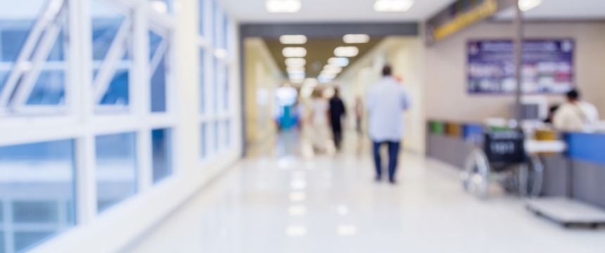 Blurred view of a hospital corridor with people walking, a wheelchair near a counter, and bright lighting from overhead fixtures—much like the busy atmosphere found in law offices or among Chicago lawyers offering litigation support.