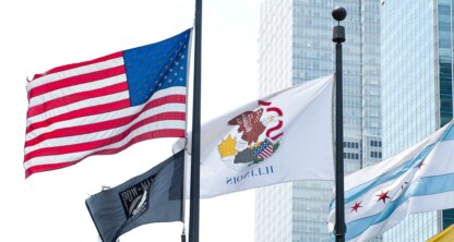 Four flags—including the U.S., Illinois state, POW/MIA, and Chicago city flags—fly on flagpoles in front of tall buildings housing law offices and lawyers in Chicago’s vibrant urban setting.