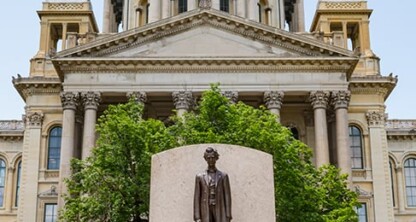 A statue of a man stands in front of a historic government building, surrounded by tall green trees—a fitting scene for lawyers in Chicago specializing in intellectual property law.