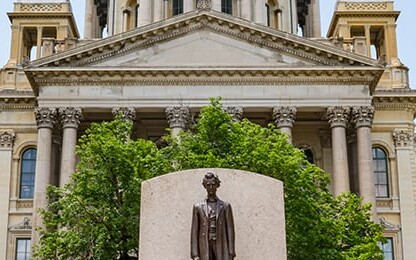A statue of a man stands in front of a historic government building, surrounded by tall green trees—a fitting scene for lawyers in Chicago specializing in intellectual property law.