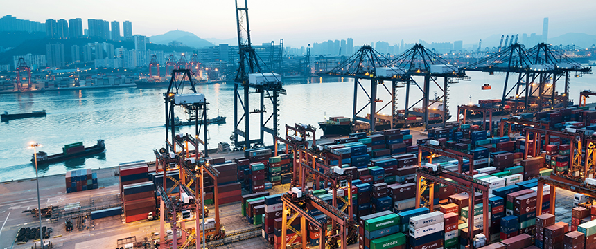 Container ships docked at a busy port with numerous shipping containers, cranes, and city buildings in the background during dusk, highlighting the global commerce that Chicago lawyers and law offices support through expert litigation support.