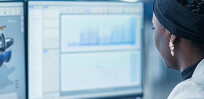 A woman sits at a desk in a law office, working on two monitors displaying technical graphics and charts—providing essential litigation support for intellectual property law cases.