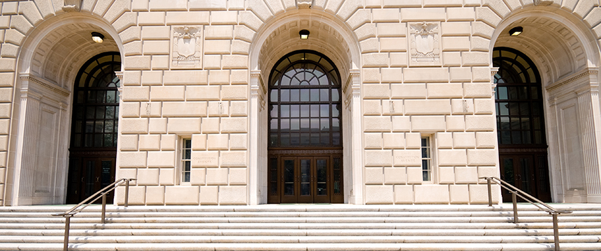 Wide stone steps lead to three large arched doorways on a beige stone building, often frequented by Chicago lawyers seeking litigation support and expertise. Decorative molding and metal railings add to its distinguished appearance.