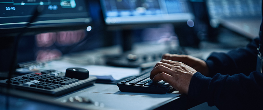 Person typing on a keyboard at a workstation with multiple computer monitors and control panels, providing litigation support services often used in law offices specializing in intellectual property law.