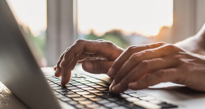 Hands typing on a laptop keyboard in a corporate law office, with natural light coming through a window—capturing the daily work of lawyers in Chicago.
