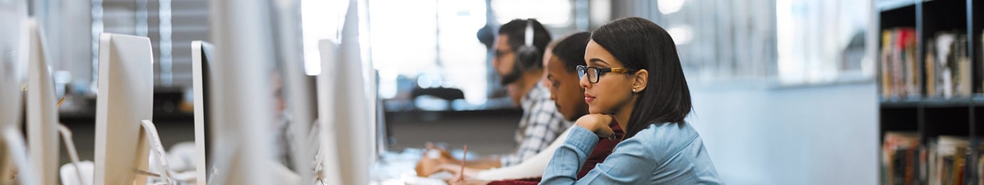 People working at desktop computers in a row at an office or computer lab, with focus on a woman in glasses in the foreground, providing litigation support for lawyers in Chicago.